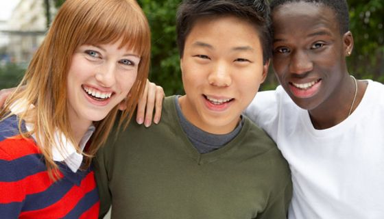 Drei junge Menschen aus unterschiedlichen Kulturen schauen lachend in die Kamera