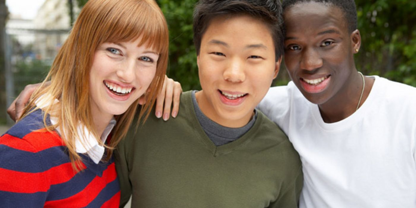 Drei junge Menschen aus unterschiedlichen Kulturen schauen lachend in die Kamera