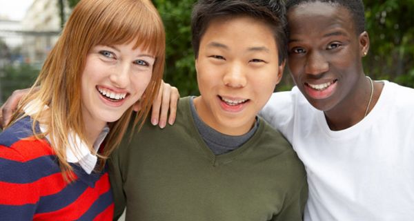 Drei junge Menschen aus unterschiedlichen Kulturen schauen lachend in die Kamera