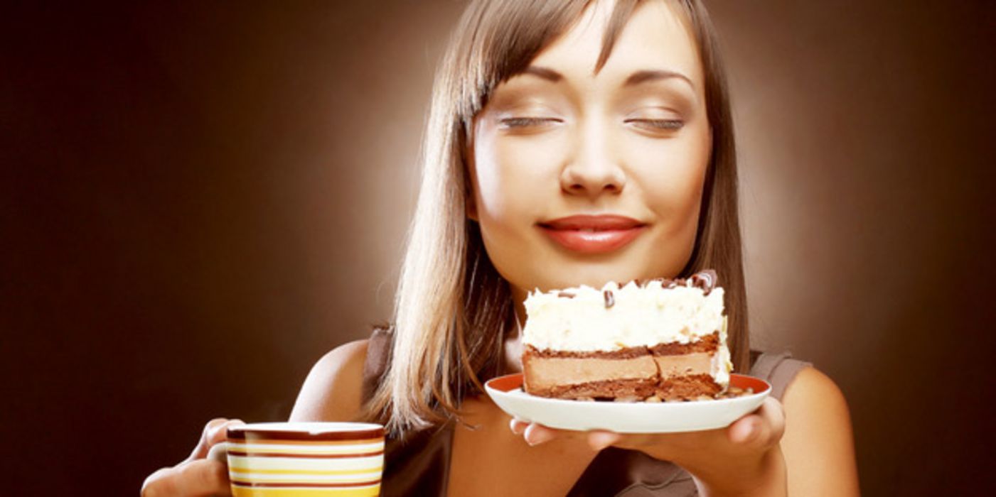 Gesicht junge, braunhaarige Frau, genussvoll lächelnd, Augen geschlossen, in der linken Hand einen Teller mit einem Stück Torte, in der anderen einen Kaffeebecher