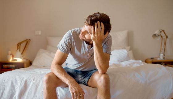 Mann sitzt erschöpft auf dem Bett.