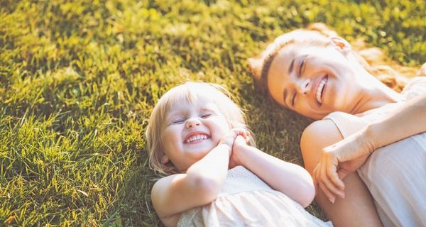 Mutter und Kleinkind liegen vergnügt im Gras.