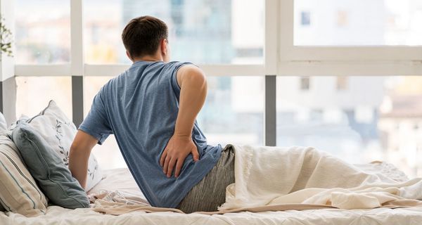 Mann hält sich im Bett den Rücken.