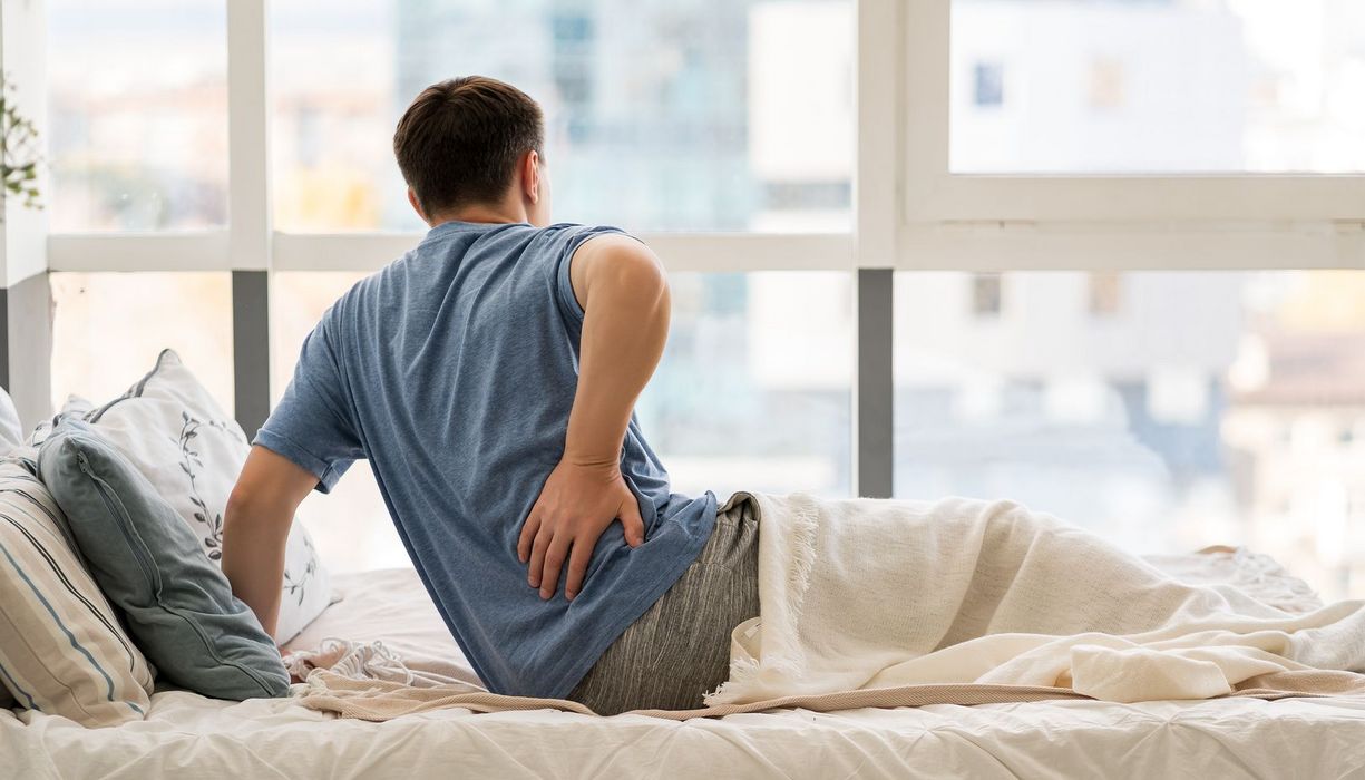 Mann hält sich im Bett den Rücken.