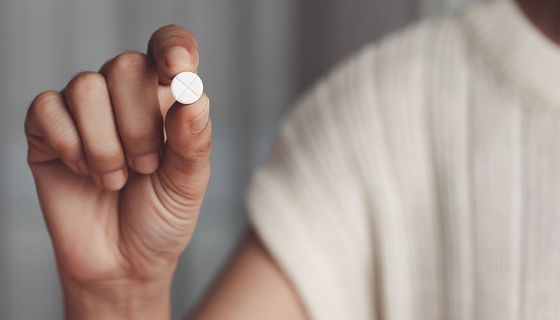 Frau, hält eine Tablette Paracetamol zwischen den Fingern.