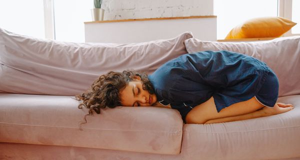 Junge Frau, liegt zusammengekrümmt auf der Couch.