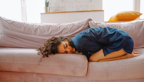 Junge Frau, liegt zusammengekrümmt auf der Couch.