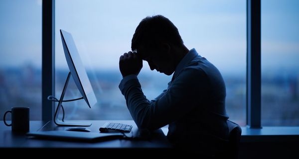 Mann, sitzt vor dem Computer im Büro und stützt den Kopf in die Hände.