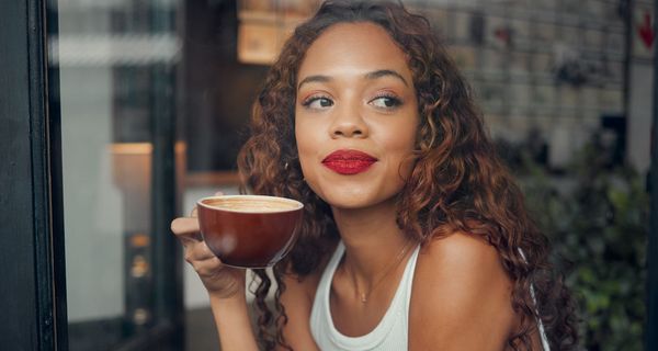 Eine junge Frau trinkt am Fenster Kaffee.