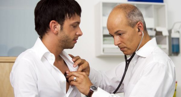 Arzt hört Mann um die 30 mit Stethoskop im Brustbereich ab