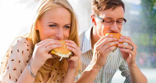 Junge Frau und junger Mann sitzen in ihrer Mittagspause im Freien und beißen herzhaft in einen Hamburger