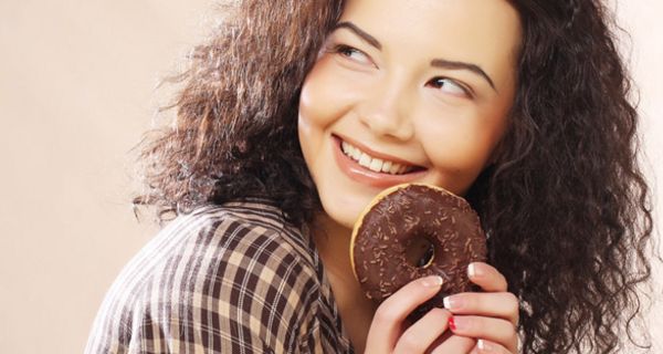 Mädchen mit dunklen Locken überlegt von einem Schoko-Donut abzubeißen
