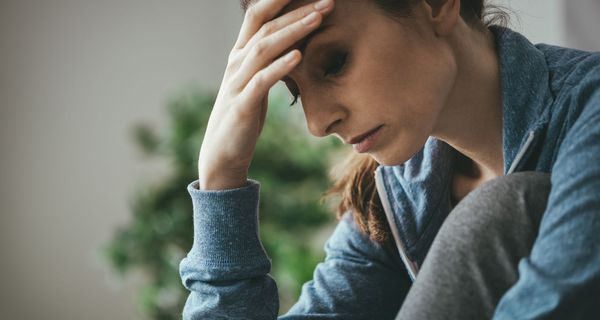 Junge Frau, stützt ihren Kopf auf die Hand und blickt traurig nach unten.