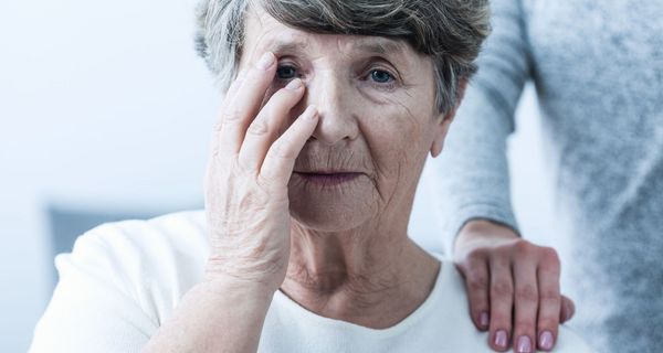 Ältere Frau, greift sich an die Schläfe und schaut traurig in die Kamera.