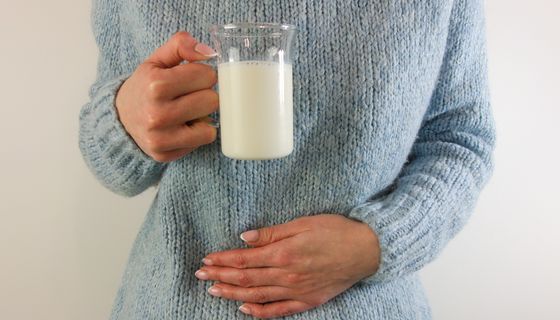 Frau, hält eine Hand an den Bauch und in einer Hand ein Glas Milch.