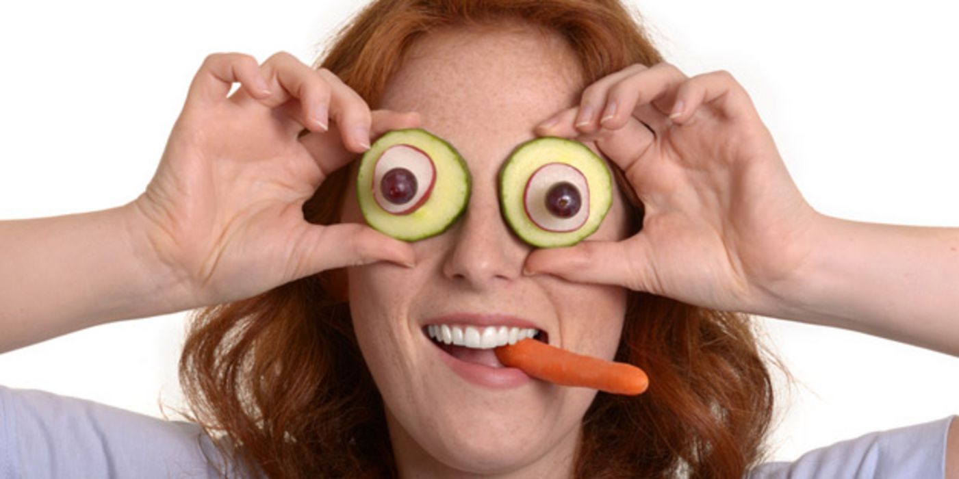 Frontalfoto Frau hält sich Scheiben von Gurke, Radieschen und dunkle Traube als "Augen" vor die Augen und hat Karotte als "Zigarette" im Mund