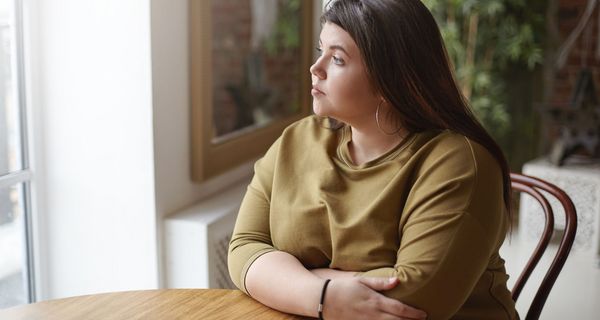 Junge übergewichtige Frau, sitzt an einem Tisch und schaut nach draußen.