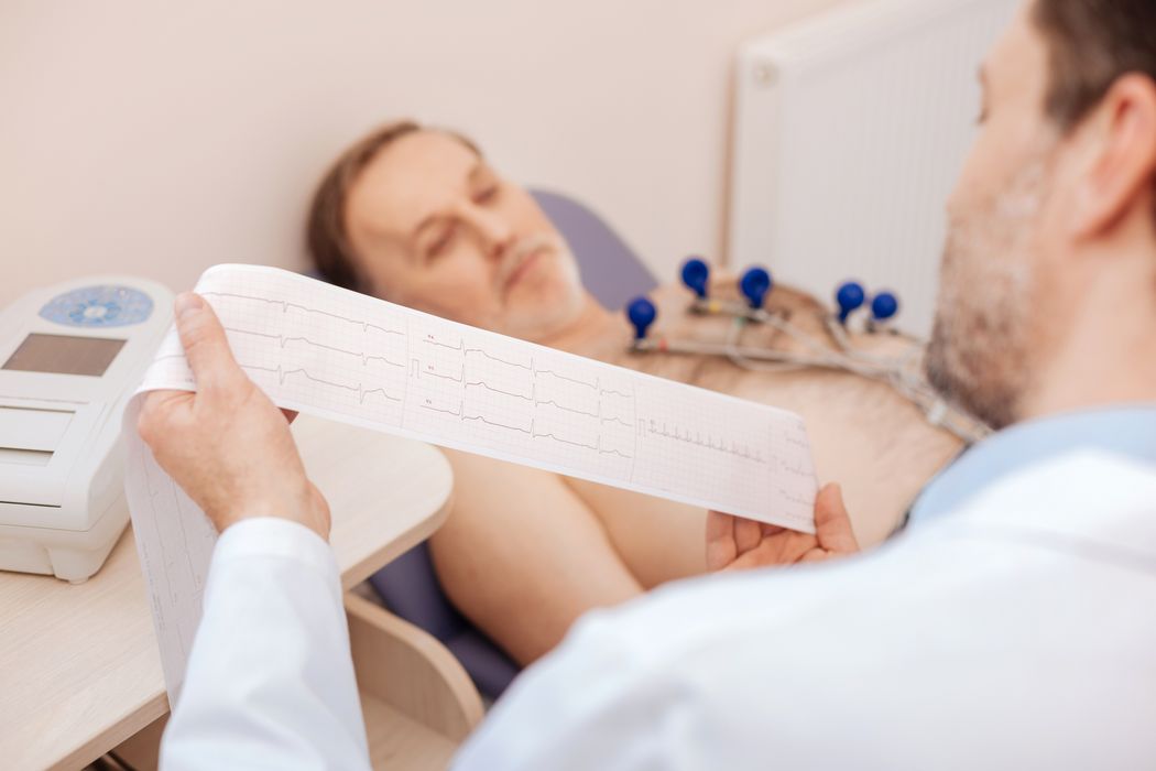 Mann liegt auf einem Krankenhausbett und Arzt liest sein EKG.
