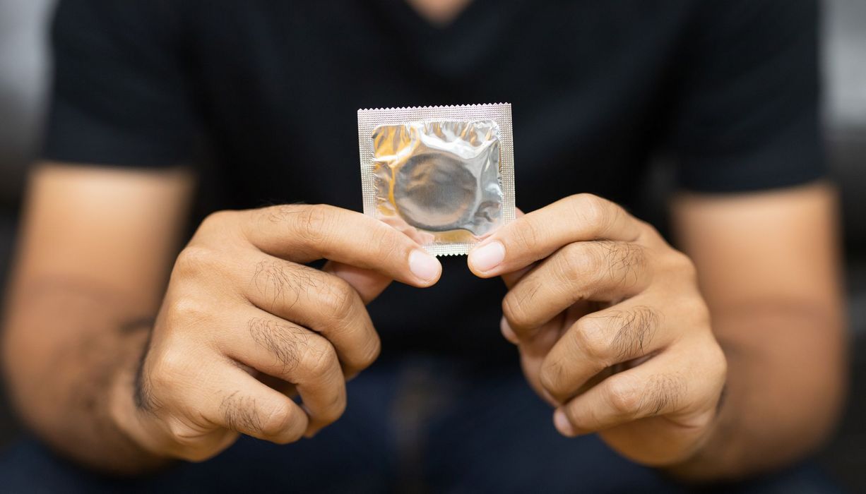 Männerhände halten ein verpacktes Kondom in den Händen.