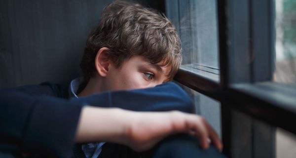 Trauriger Junge mit leerem Blick sitzt am Fenster.