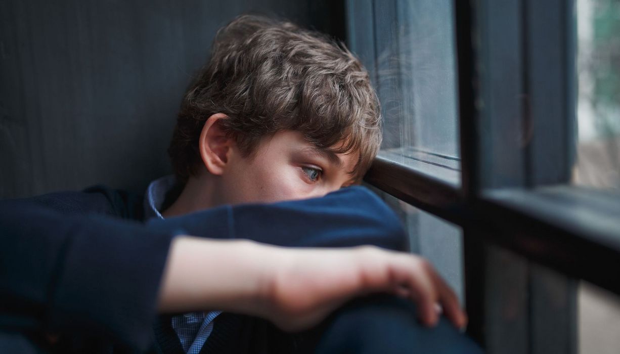 10-jähriger Junge, schaut traurig aus dem Fenster.