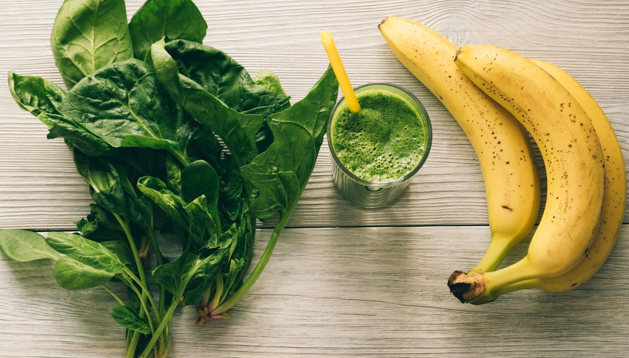 Spinat, ein grüner Smoothie und Bananen auf einem hellen Hintergrund.