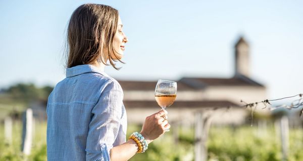 Junge Frau, steht zwischen Weinreben mit einem Glas Wein.