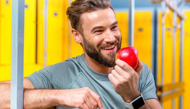 Junger Mann mit Vollbart isst einen Apfel.