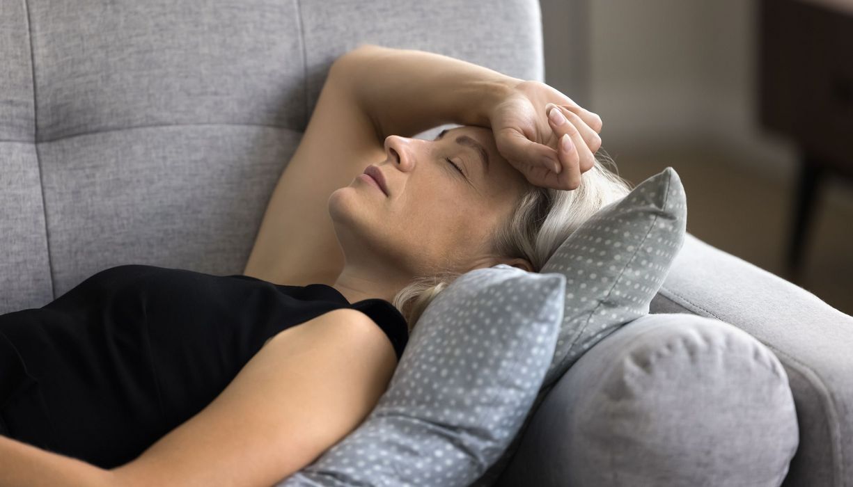 Frau, liegt erschöpft auf der Couch.