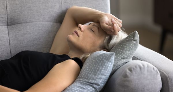 Frau, liegt erschöpft auf der Couch.