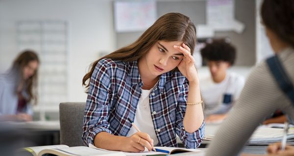 Schülerin sitzt in der Klasse und hält sich den Kopf.