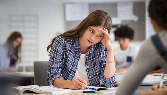 Schülerin sitzt in der Klasse und hält sich den Kopf.