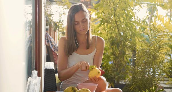 Eine Frau sitzt an einem Tisch im Garten und schält Mangos.