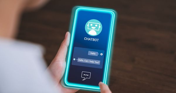 Blick auf ein Smartphone mit einer geöffneten Chatbot-App: Der Bot hat geschrieben: "Hello" und "Can I help you?"