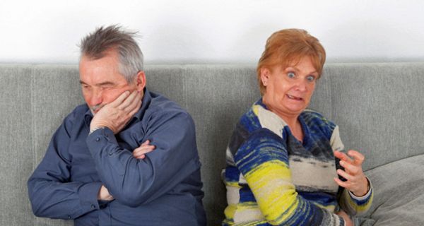 Senioren-Paar auf einer Couch; er schmollt, sie regt sich auf