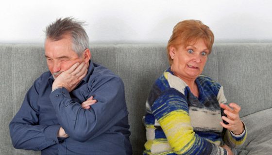 Senioren-Paar auf einer Couch; er schmollt, sie regt sich auf