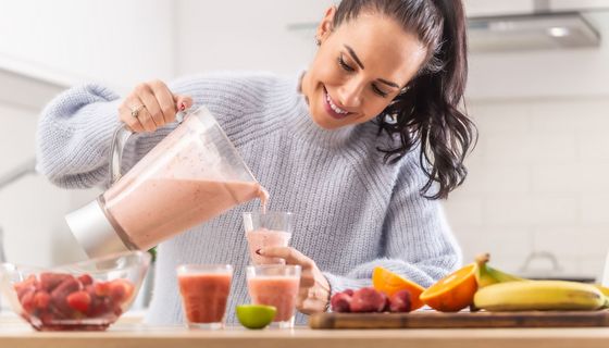 Junge Frau, schenkt sich einen selbstgemachten Smoothie aus einem Mixer ein.