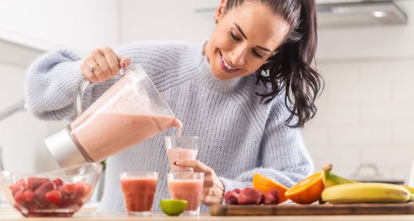 Junge Frau, schenkt sich einen selbstgemachten Smoothie aus einem Mixer ein.