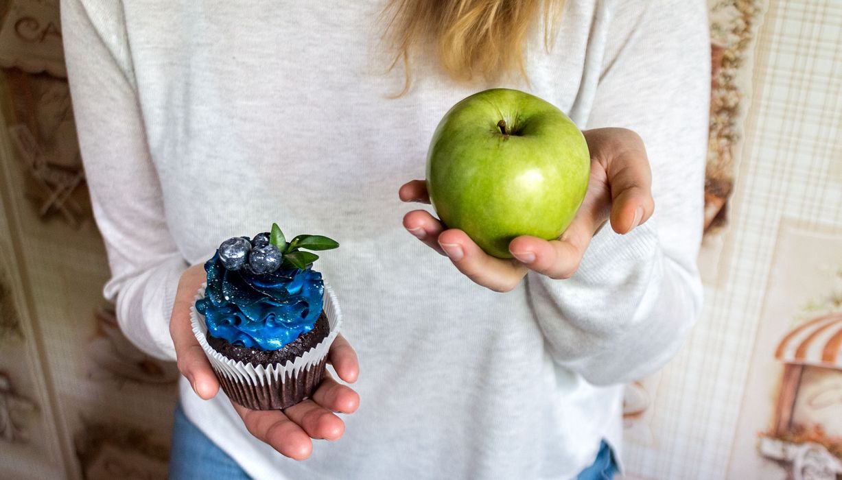 Frau hält einen Apfel und einen Muffin in den Händen.