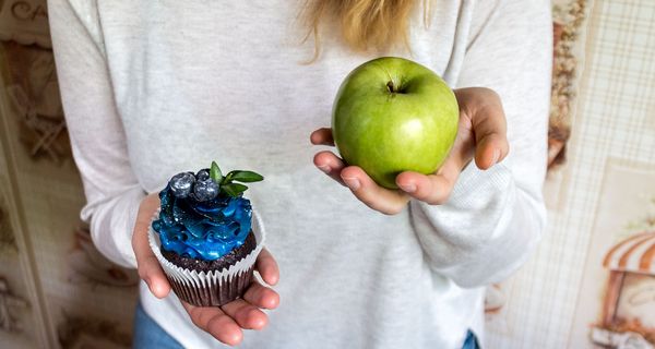 Frau hält einen Apfel und einen Muffin in den Händen.