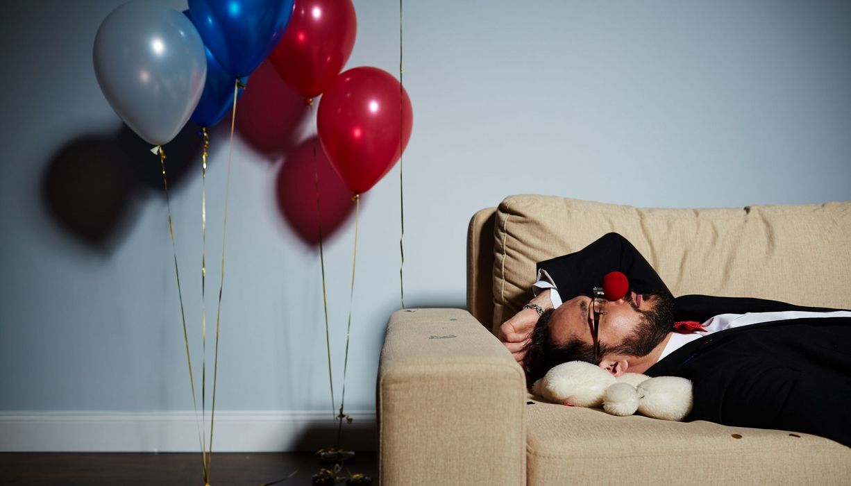 Mann, liegt nach einer durchzechten Nacht auf der Couch und schläft.