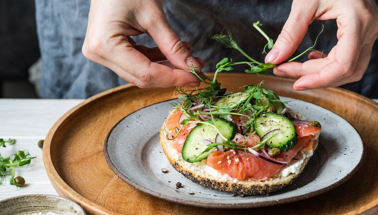 Frau, bereitet sich ein Brötchen mit Lachs zu.