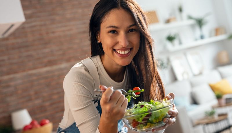 Junge Frau isst einen Salat mit Tomaten und Mais.