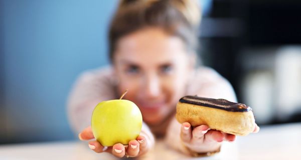 Frau hält Apfel und Schokobrötchen in der Hand.