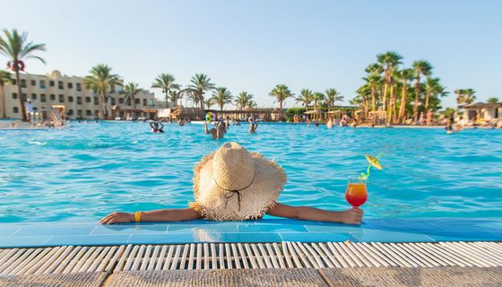 Frau sitzt mit Cocktail in der Hand im Pool und schaut in den blauen Himmel