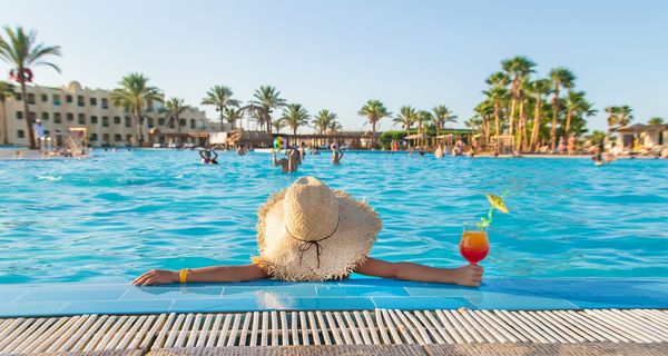 Frau sitzt mit Cocktail in der Hand im Pool und schaut in den blauen Himmel