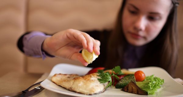 Junge Frau träufelt Zitronensaft auf eine Fischgericht.