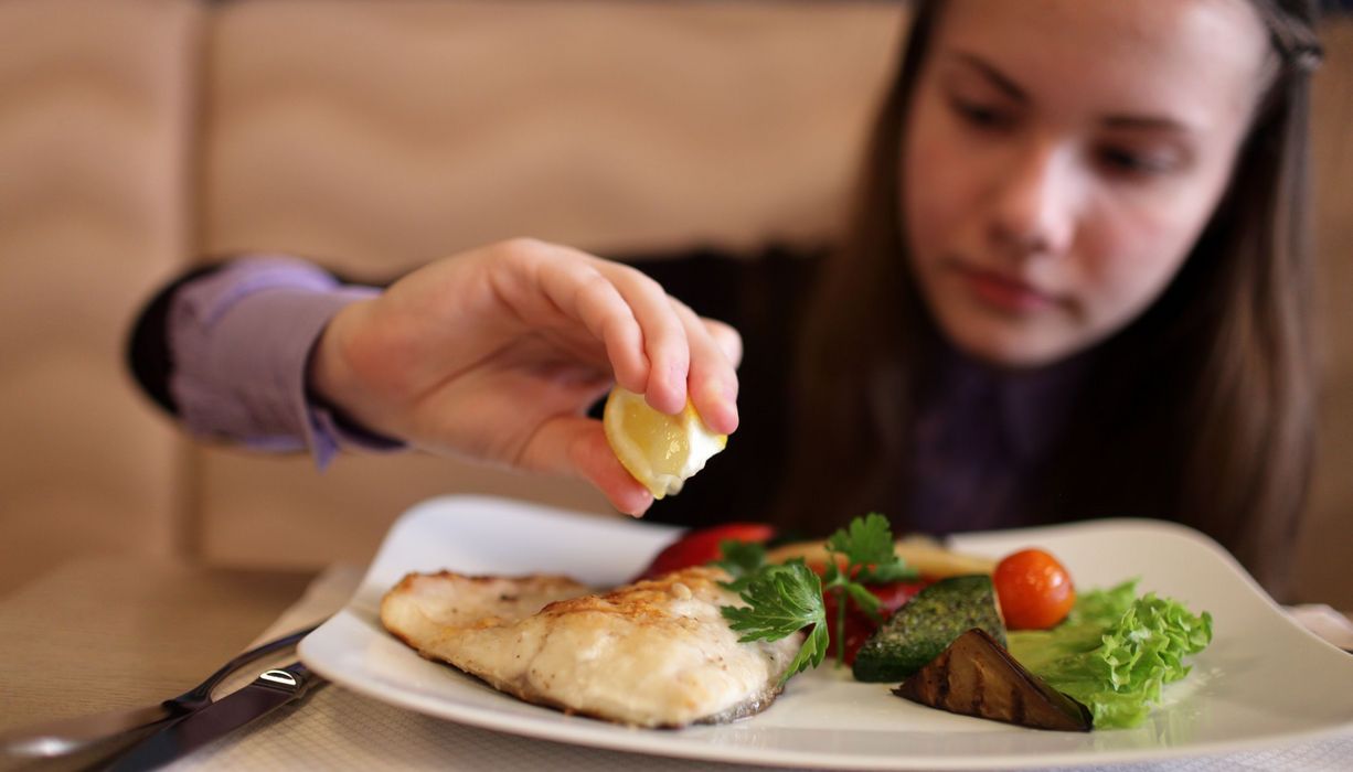 Junge Frau träufelt Zitronensaft auf eine Fischgericht.
