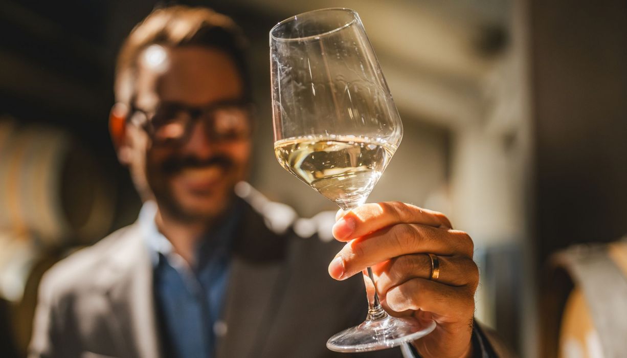 Mann, hält ein Glas Wein in der Hand.
