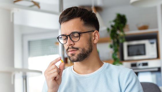 Junger Mann schaut kritisch eine Tablette an.
